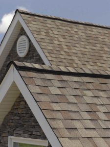 Close-up view of home with brown asphalt shingle roofing. Blue sky in background.