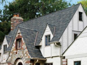 Large home with white exterior walls and gray asphalt shingle roofing. Trees in background.