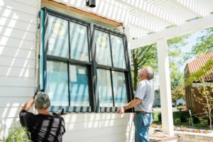 Two craftsmen installing new window on home. Sunny day