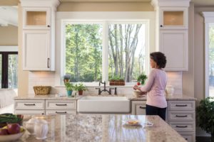 Adult female standing in kitchen admiring newly installed replacement windows.