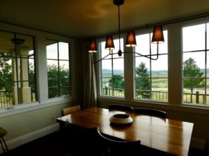 Dining room with dim lighting, wooden dining table, and five large vinyl windows.