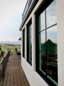 View of home's exterior featuring a wraparound porch and large black frame windows overlooking mountainous scenery.