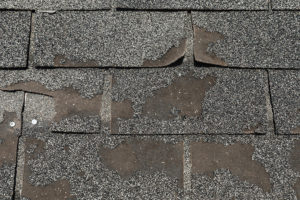 Close up of damaged asphalt roofing shingles in need of repair